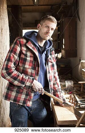A man using a hand saw on a plank in a workshop View Large Photo Image Stock Photo - A man using a hand saw on a plank in a workshop. Fotosearch