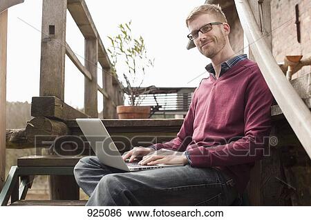 A man with a laptop sitting on a staircase View Large Photo Image Stock Photograph - A man with a laptop sitting on a staircase. Fotosearch