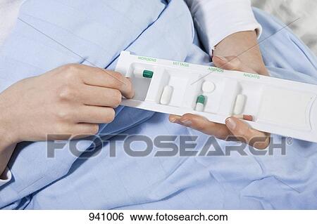 A patient in a hospital bed taking a pill from a pill organizer, focus on hands View Large Photo Image Stock Photograph - A patient in a hospital bed taking a pill from a pill organizer, focus on hands. Fotosearch