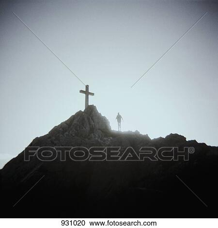 Stock Image - A person standing below a crucifix on a mountain top, Mount Saint Michel, Normandy, France. Fotosearch