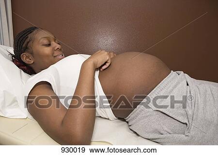 A pregnant woman lying on an exam table smiling down at her abdomen View Large Photo Image Stock Photo - A pregnant woman lying on an exam table smiling down at her abdomen. Fotosearch