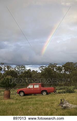 Stock Image - A rainbow in the sky above a pick-up truck in a field. Fotosearch