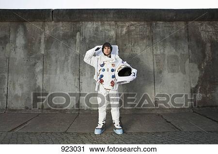 Stock Image - A saluting astronaut standing on a sidewalk in a city. Fotosearch