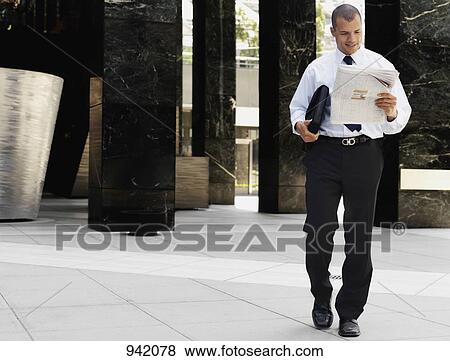 A smiling businessman walking and reading the newspaper View Large Photo Image Stock Photo - A smiling businessman walking and reading the newspaper. Fotosearch