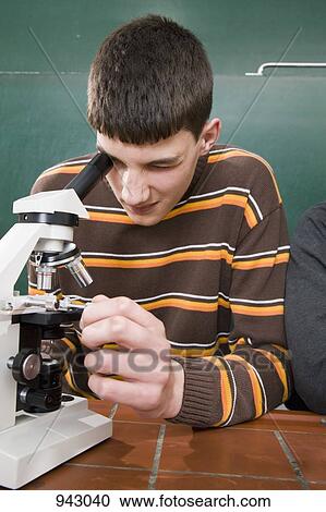 Stock Image - A student looking through a microscope in biology class. Fotosearch