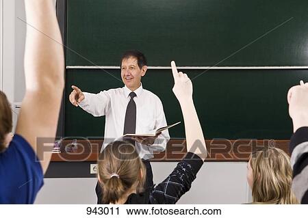 Stock Image - A teacher points while his students raise their hands in a classroom. Fotosearch