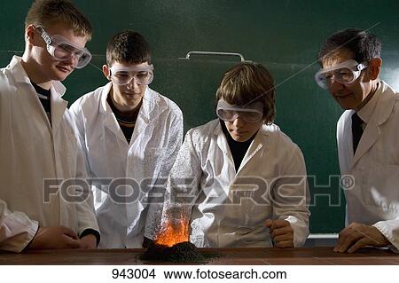 Picture - A teacher supervising students doing a chemistry experiment with lit gunpowder. Fotosearch