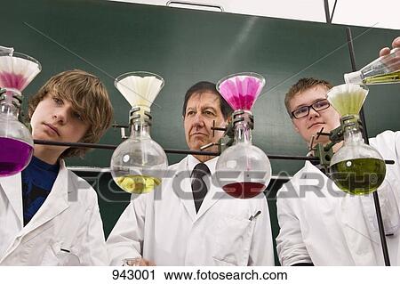 Stock Image - A teacher supervising two students conducting a chemistry experiment. Fotosearch