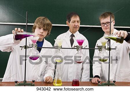 Stock Image - A teacher supervising two students conducting a chemistry experiment. Fotosearch