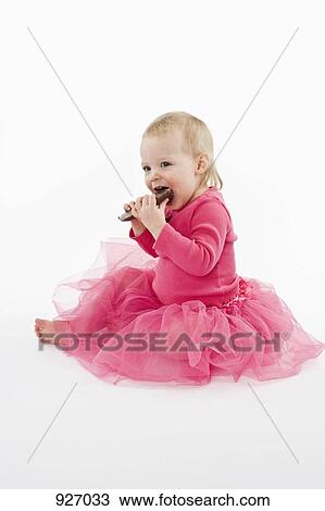 Stock Image - A toddler wearing a tutu and eating chocolate. Fotosearch