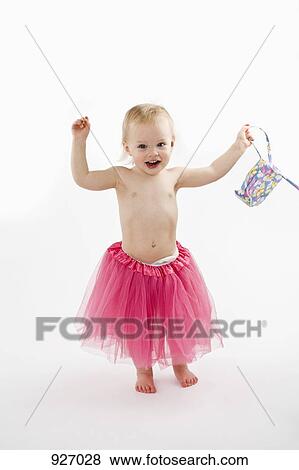 Stock Photo - A toddler wearing a tutu and holding a purse, studio shot. Fotosearch