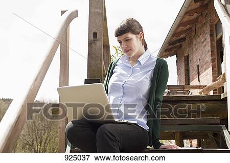A woman sitting on a staircase, looking at a laptop View Large Photo Image Stock Photo - A woman sitting on a staircase, looking at a laptop. Fotosearch