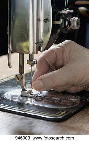 Stock Image - A woman threading a needle on a sewing machine, detail of hand. Fotosearch