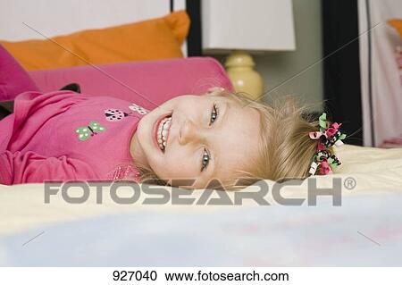 Stock Image - A young girl lying on a bed, portrait. Fotosearch