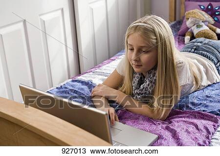 A young girl lying on her bed, using a laptop View Large Photo Image Stock Image - A young girl lying on her bed, using a laptop. Fotosearch