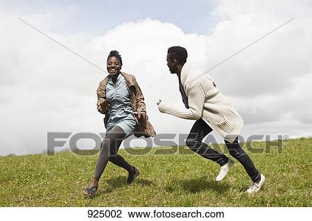 Stock Image - A young man chasing his girlfriend down a hill. Fotosearch