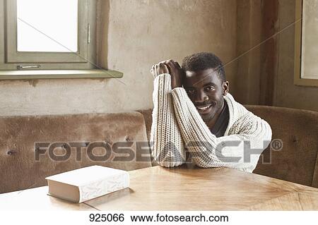 A young man sitting at a table View Large Photo Image Stock Photograph - A young man sitting at a table. Fotosearch