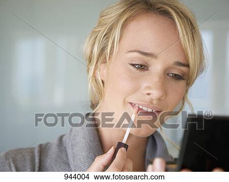 Picture - A young woman applying lip gloss. Fotosearch