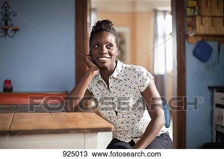 A young woman sitting at a table in a domestic kitchen View Large Photo Image Stock Image - A young woman sitting at a table in a domestic kitchen. Fotosearch