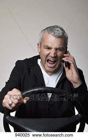 An angry man using a mobile phone behind a car steering wheel View Large Photo Image Stock Photography - An angry man using a mobile phone behind a car steering wheel. Fotosearch