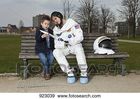 An astronaut and a boy sitting on a park bench looking at a model rocket View Large Photo Image Stock Photo - An astronaut and a boy sitting on a park bench looking at a model rocket. Fotosearch