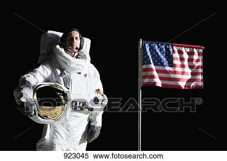 Stock Photography - An astronaut holding his helmet standing next to an American flag, portrait. Fotosearch