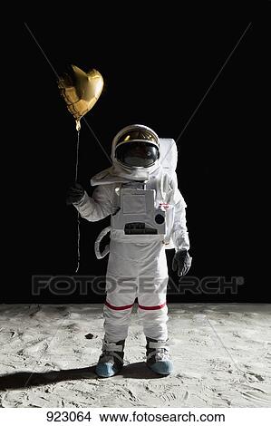 Picture - An astronaut on the moon holding a heart shaped helium balloon. Fotosearch