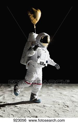 Stock Photograph - An astronaut on the moon holding a heart shaped helium balloon. Fotosearch