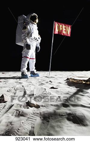 Stock Image - An astronaut on the moon next to a flag with OPEN on it. Fotosearch
