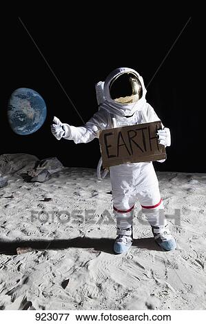 Stock Photo - An astronaut on the moon with his thumb out, holding 'EARTH' sign. Fotosearch