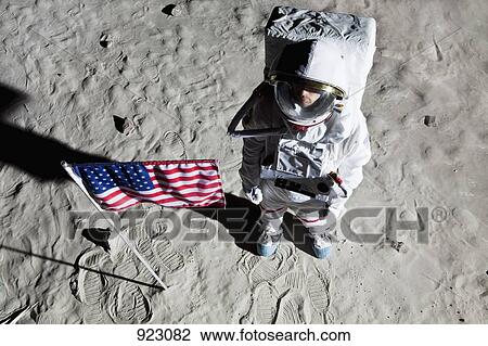 Stock Image - An astronaut on the surface of the moon next to an American flag. Fotosearch