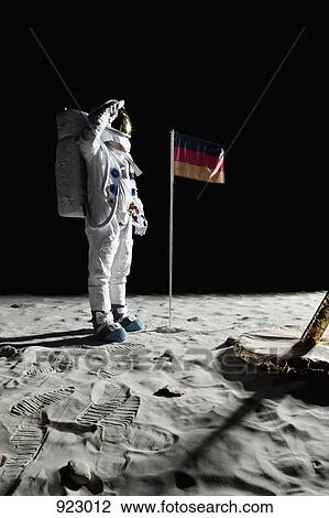Stock Image - An astronaut standing near a lunar lander salutes an German flag. Fotosearch
