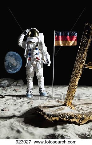 Stock Photo - An astronaut standing near a lunar lander salutes an German flag. Fotosearch