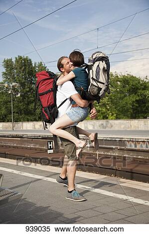 Stock Photography - An ecstatic woman hugs her boyfriend on a train platform. Fotosearch