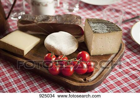 Picture - Cheese, tomatoes and cured ham on a wood cutting board. Fotosearch