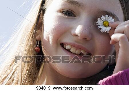 Close-up of a girl holding a flower over her eye View Large Photo Image Stock Photo - Close-up of a girl holding a flower over her eye. Fotosearch
