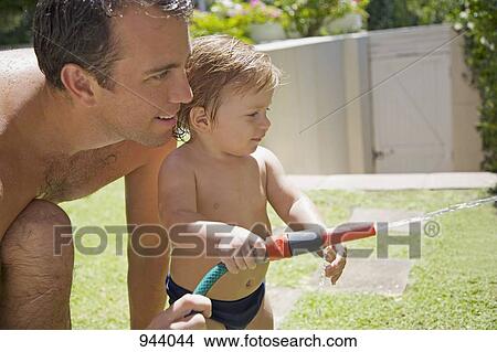 Picture - Detail of a man and a baby boy with a garden hose. Fotosearch