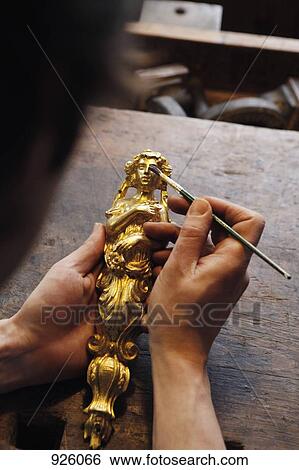 Stock Photograph - Detail of a person holding a gilded figurine and a paint brush. Fotosearch