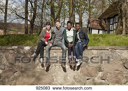 Stock Image - Four friends sitting on a stone wall. Fotosearch