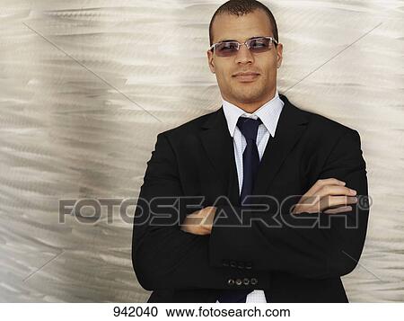 Stock Image - Portrait of a businessman with his arms crossed, wearing sunglasses . Fotosearch