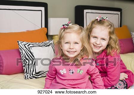 Portrait of two sisters sitting on a bed View Large Photo Image Picture - Portrait of two sisters sitting on a bed. Fotosearch