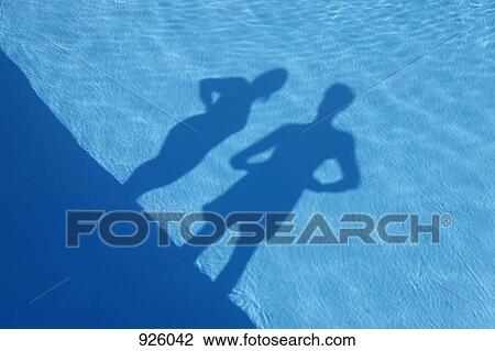 Stock Image - Shadows of a man and a woman standing at the edge of a swimming pool. Fotosearch
