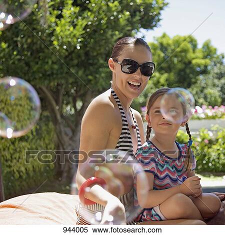 Soap bubbles floating by a mother and daughter sitting together outdoors View Large Photo Image Stock Photography - Soap bubbles floating by a mother and daughter sitting together outdoors. Fotosearch