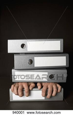 Stock Image - The hands of a man between a stack of folders. Fotosearch
