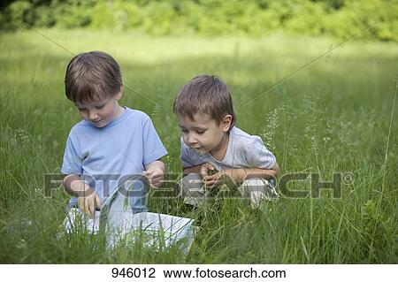 Two boys looking at a book in a field View Large Photo Image Stock Image - Two boys looking at a book in a field. Fotosearch