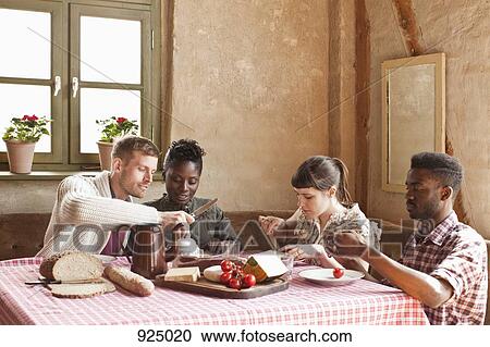 Stock Image - Two couples having a simple rustic meal together. Fotosearch