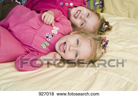 Two sisters lying on a bed, laughing View Large Photo Image Stock Photo - Two sisters lying on a bed, laughing. Fotosearch