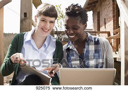 Stock Photography - Two women looking at a clipboard and laptop. Fotosearch