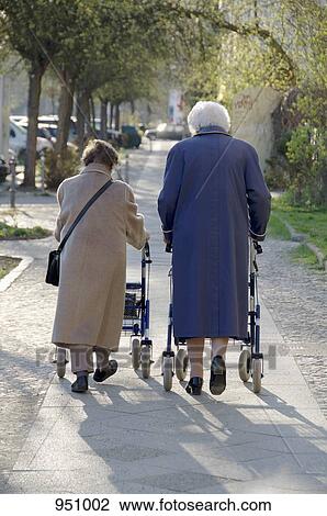 Two women using walkers to walk together on a sidewalk, rear view View Large Photo Image Stock Image - Two women using walkers to walk together on a sidewalk, rear view. Fotosearch