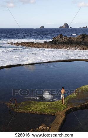 Stock Photograph - View of a boy standing by rock pools. Fotosearch